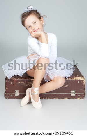 Ballerina children dancer sitting on an old suitcase, gray background