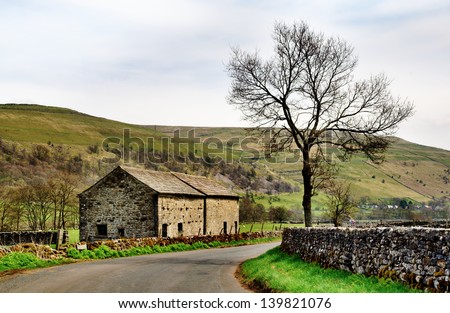 A stone built barn and solitary tree at the side of a country lane in the Yorkshire Dales, England, set again a backdrop of fells