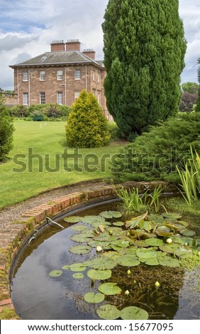 An ornamental pond in a country estate garden with a large house in the background