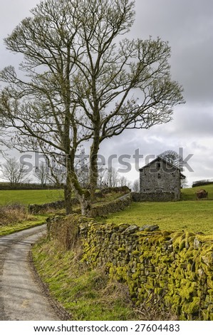English country lane with stone barn building in background.