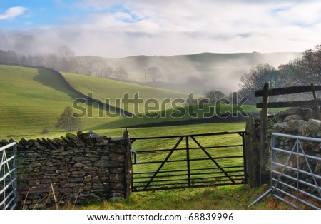 A view of rolling English Countryside near Staveley, Cumbria. Mist i the distance, and a gate and dry-stone wall in the foreground