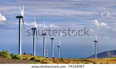 Scenic view of turbines on wind farm in countryside with sea and cloudscape background.