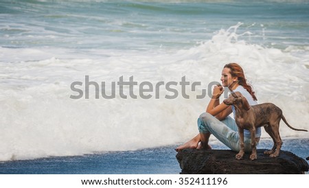 You woman sitting on rock on beach with her puppy