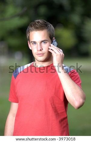 Picture of young leisure time dressed man with cell phone in park talking while walk