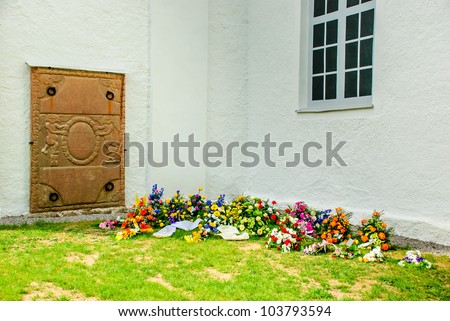 Funeral flowers put in shade beside old church