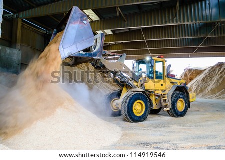Front loader emptying wood chips in pile for use in pellets manufacturing.