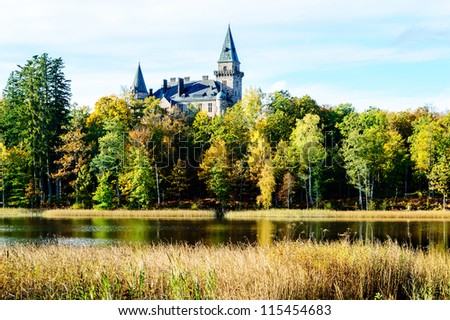 Castle in scenic view surrounded by forest in autumn. Lake in foreground. Castle was built and given as wedding gift.