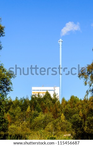 District heating and power plant using bio fuel to produce heat and electricity. Tall chimney emitting some water vapor and smoke. The plant is surrounded by forest.