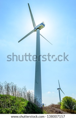 Wind turbine against blue sky. Wind power is the conversion of wind energy into a useful form of energy. Here is two turbines. One is blocking the sun.