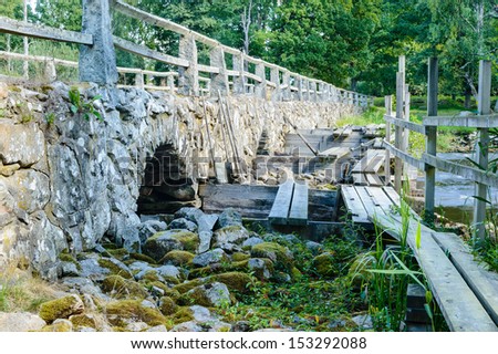 A temporary walkway beside old stone bridge over running water.
