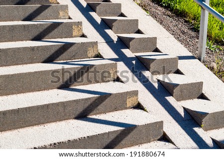 Shadow and light makes zigzag pattern on stone stairs. Small patch of green grass in corner.