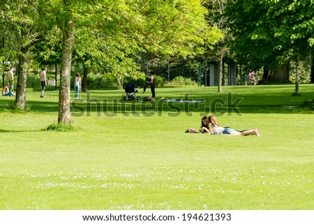 RONNEBY, SWEDEN - MAY 24, 2014: Two girls talking in public park. Green grass and sunshine. Active people in background.
