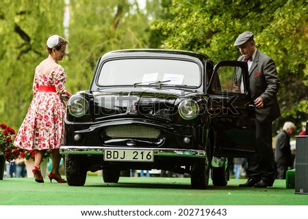 RONNEBY, SWEDEN - JUNE 28, 2014: Nostalgia Festival with classic cars and motorcycles as main attractions. Black Standard 8 classic car. Owners in contemporary clothing on stage by the car.