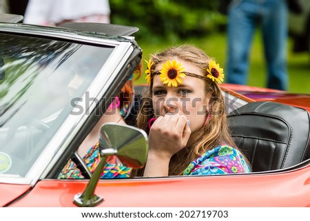 RONNEBY, SWEDEN - JUNE 28, 2014: Nostalgia Festival with classic cars and motorcycles as main attractions. Young female dressed as hippie or flower power girl in red cab.