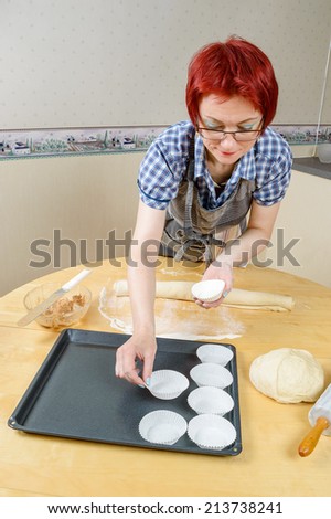 Red haired woman place paper baking cups on steel baking sheet.