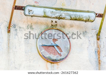 Old broken clock on industrial wall. Cover is broken and time has stopped. Place for text beside clock. Fluorescent light above clock is also broken.