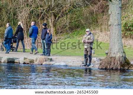 MORRUM, SWEDEN - MARCH 28, 2015: Premiere day for trout and salmon fishing. Spectators walk by and look while people fish. Senior man stand by tree while fishing.