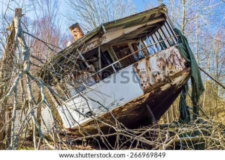 Stern of old shipwrecked passenger boat all the way up into the forest where it has been pulled to its final resting place. Nature is closing in with trees and broken branches all over.