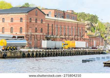 KARLSHAMN, SWEDEN - MAY 06, 2015: Trucks parked outside historic brick factory building waiting to unload their cargo. Unknown worker walking outside. Water in foreground.