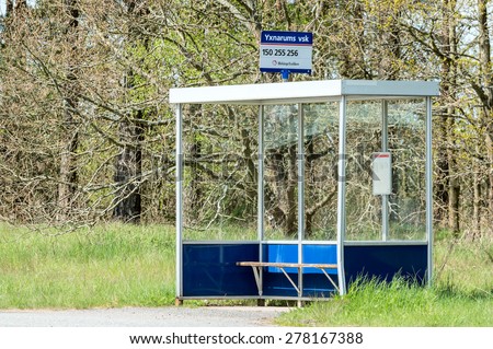 YXNARUM, SWEDEN - MAY 11, 2015: Empty bus stop shelter with small bench. Forest in background and high grass at sides. Sign on top of shelter with bus numbers and place name.