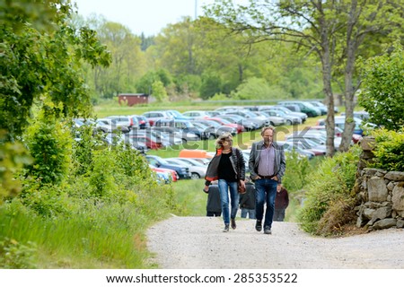 BJORKERYD, SWEDEN - JUNE 07, 2015: People walking from car park in farmers field. Here is one couple walking towards the camera. Cars out of focus in background.