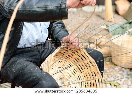 Unknown person making a wooden basket by hand. The wood is weaved into steel wires. Person is sitting down while working.
