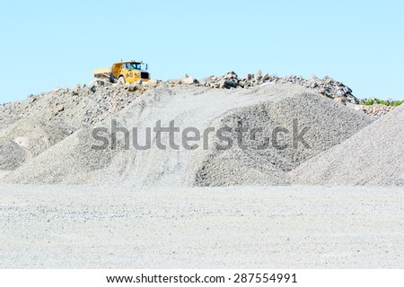 Yellow tractor with trailer on top of large gravel mound.