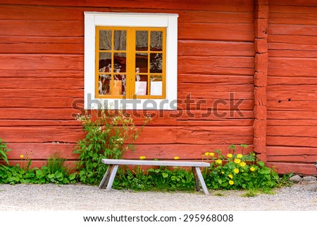 Old unpainted wooden bench under a white window on red house.
