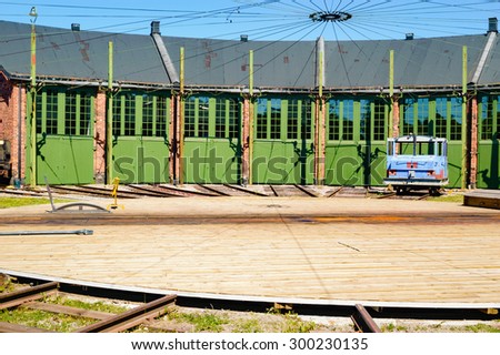 Green doors side by side on a train service depot. Rotating disk with railroad track on in the foreground. Disk is made of wood and directs the trains to the doorways. Small blue towing engine outside