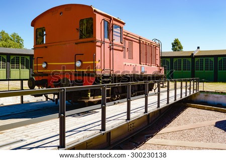 A red diesel train standing on a rotating switch. The switch is used to maneuver the trains so they can be driven in through the correct door on the service building in the background.
