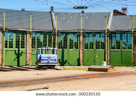 Green doors side by side on a train service depot. Rotating disk with railroad track on in the foreground. Disk is made of wood and directs the trains to the doorways. Small blue towing engine outside