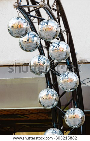 Several disco balls, mirror balls or glitter balls hanging on a stand outside a nightclub. Daytime photo.