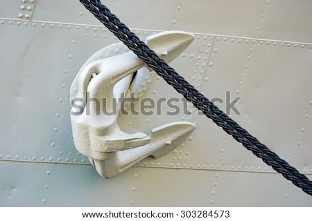 White anchor and black rope on white metal ship.