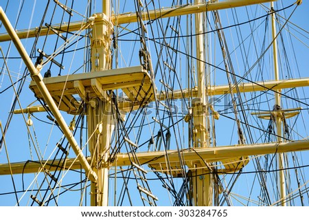 Abstract pattern of sailing ships masts, working platforms and ropes. Yellow details against clear blue sky.
