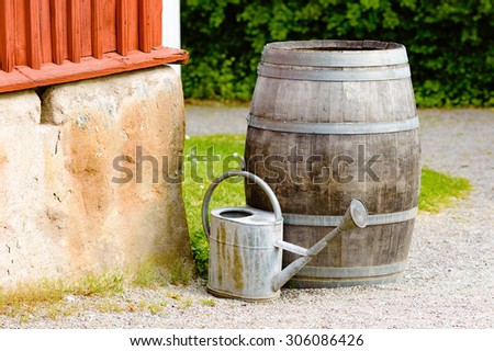 Old wooden barrel standing in a corner of an old house to collect water. Water can standing in front ready to be used as soon as there is water in barrel. Old and rough, vintage feel to it.