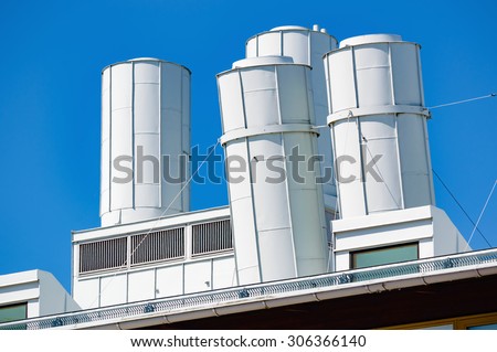 Air vents on top of an industrial building. Some of the vents are slightly tilted. White metal against a clear blue sky.