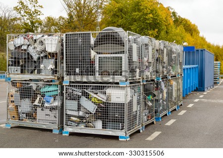 Netted bins full of discarded electronics waste waiting to be transported to the recycle plant for further processing. Blue containers in background.