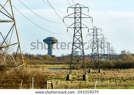 Power lines and a water tower in the background. Water and power are essential for every modern society. Power lines stretch over some wetland toward the city. Houses are visible behind some trees.