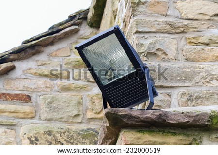Home security light outdoor on the corner of a stone cottage. Metal halide floodlight enclosure.