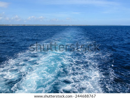 Ship or boat wake in a tropical sea looking back at a tropical holiday island - concept of departure or going home