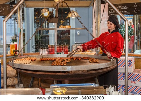 Manchester,England - November 16th: German sausages cooking on a huge swinging grill at the Manchester 2015 Christmas market.  The sausages are being cooked by a  girl in red traditional costume.