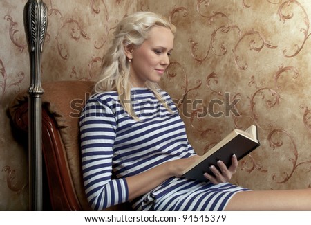 Young and beautiful girl reading a book cover in black sitting on a couch in his home
