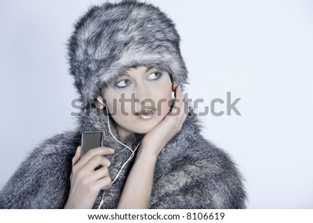 studio shot portrait of a beautiful woman russian type in a fur coat and hat studio shot portrait of a beautiful woman russian type in a fur coat and hat using her multimedia player listening music