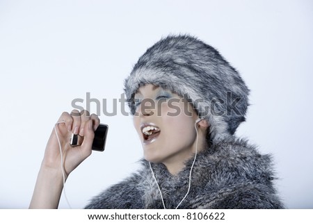 studio shot portrait of a beautiful woman russian type in a fur coat and hat using her multimedia player as a microphone and singing