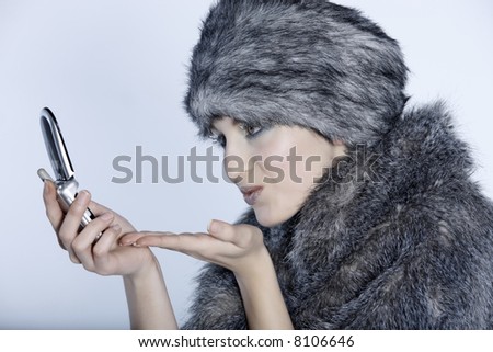 studio shot portrait of a beautiful woman russian type in a fur coat and hat kissing and saying hello by cellphone
