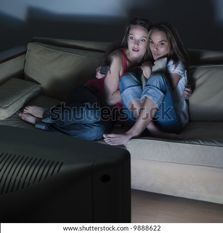 pictures in a living room of two young girls sitting on a couch watching on tv a scary movie