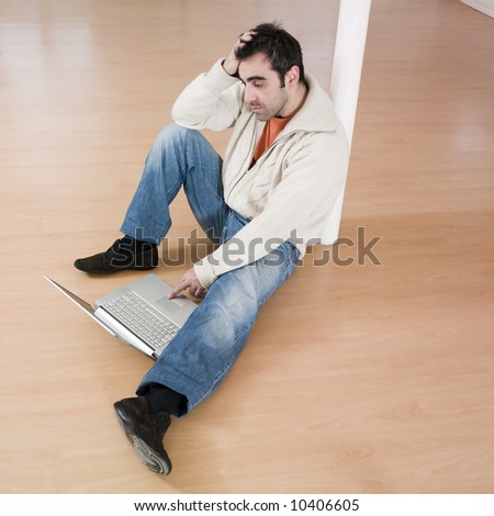 man sitting on the floor inside an empty loft appartement with tax forms and laptop computer