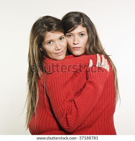 studio shot portrait on isolated background of two sisters twin women friends holding in arms each other
