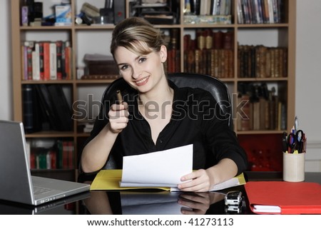 cute and smiling businesswoman at the office desk pointing his pen as his finger at you