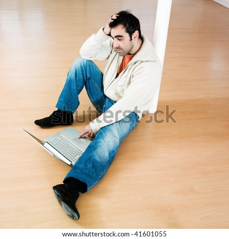 man sitting on the floor inside an empty loft apartment with tax forms and laptop computer